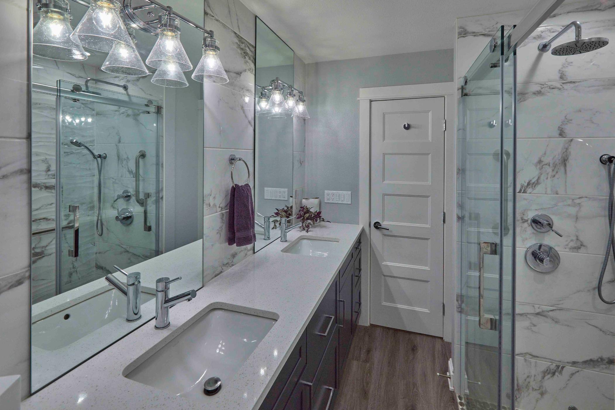 Remodeled basement bathroom view of jack and jill sinks, with partial view of walk-in shower in Tigard, OR by Creekstone Design + Remodel