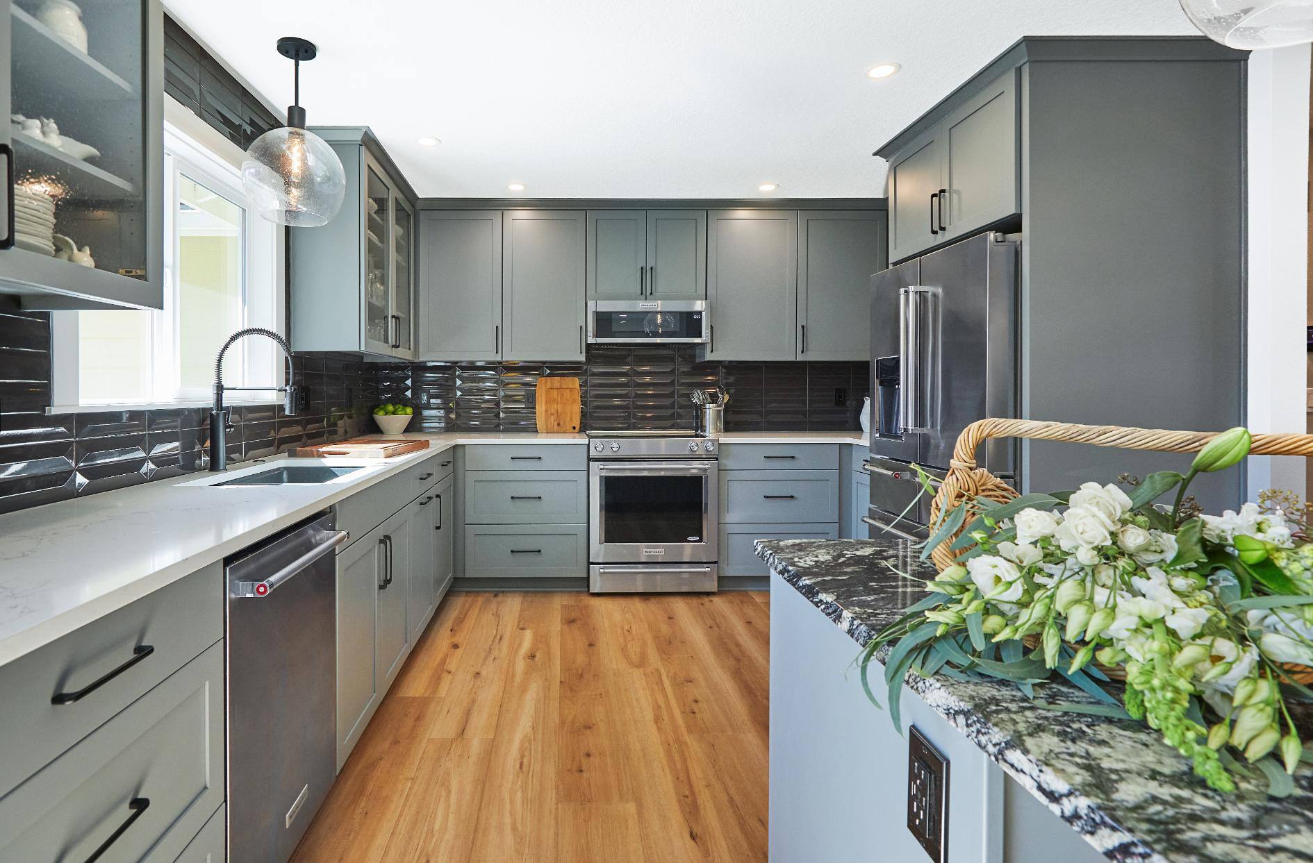 Full view of remodeled kitchen with gray cabinetry, light wood floors, and black backsplash in Tigard, OR by Creekstone Design + Remodel